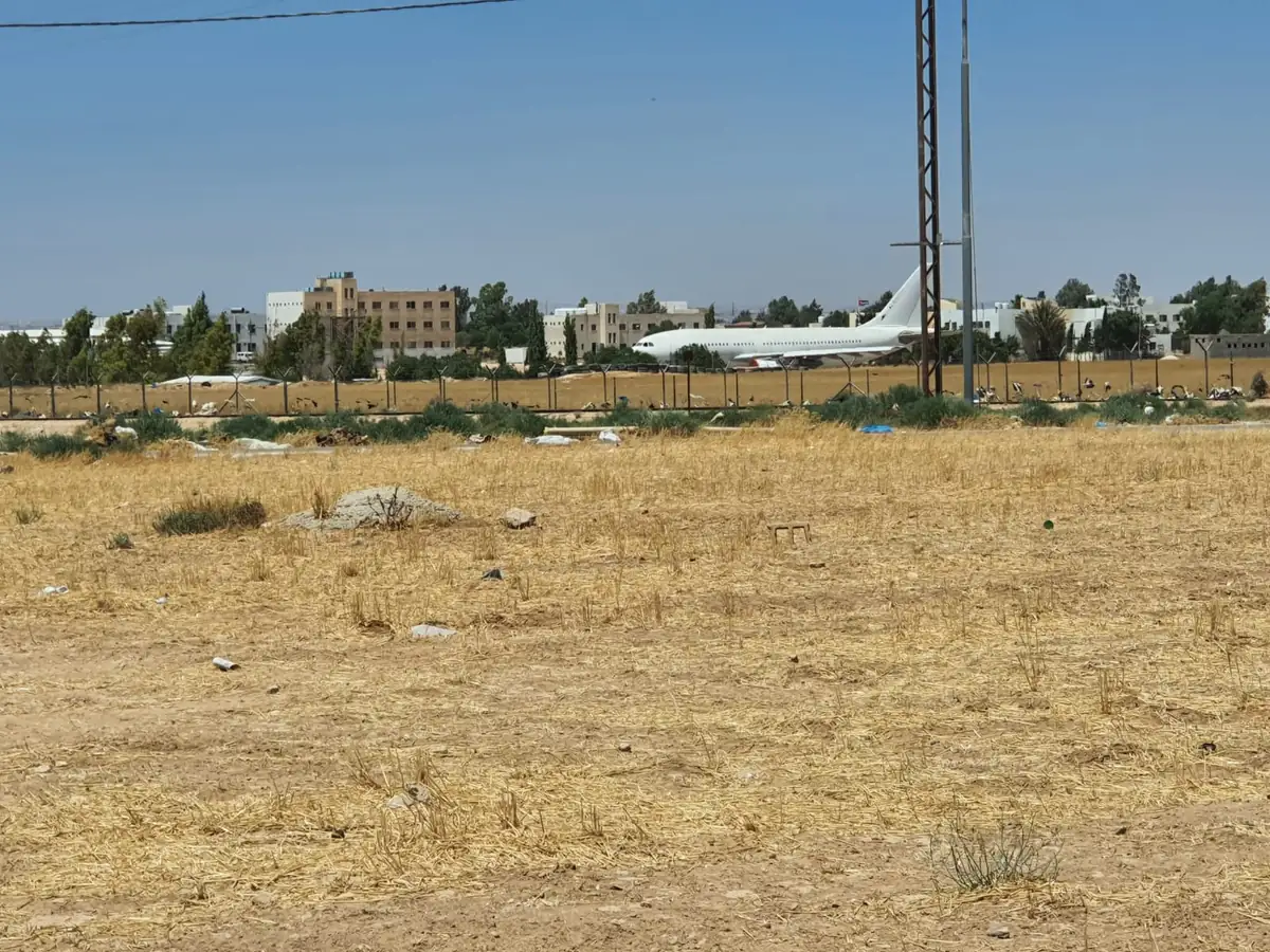 أرض في الجيزة تحدّها شبكة سياج وخلفها منشآت ومبانٍ