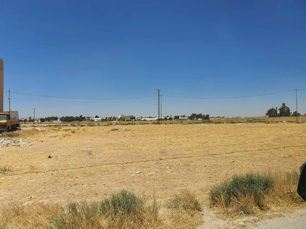 أرض مفتوحة في الجيزة مع أعمدة كهرباء ومبانٍ ومنشآت في الخلفية